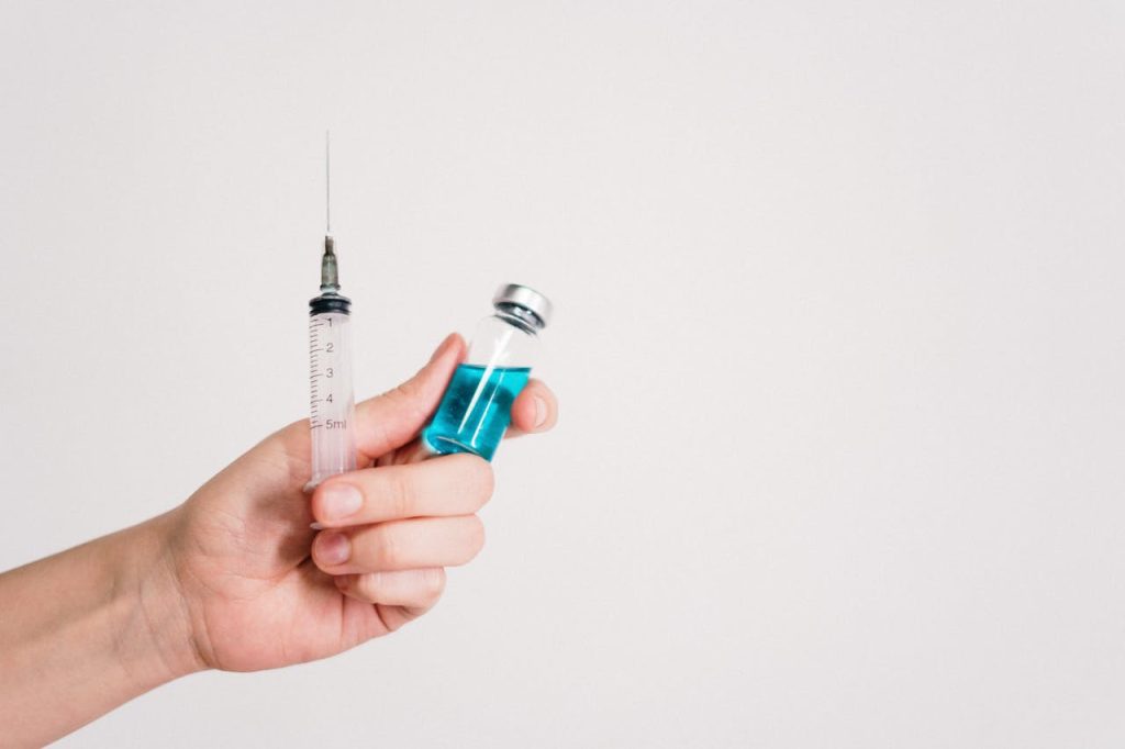 Crafting Captivating Headlines: Your awesome post title goes here Hand holding a syringe and vaccine vial on a white background, symbolizing healthcare and immunization.